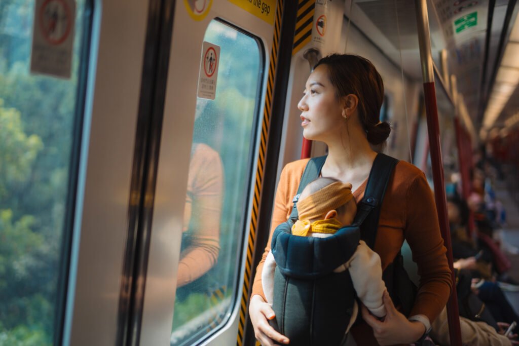 young asian working mother carrying her baby girl in a baby carrier, riding on subway commuting in the city. travelling with a baby. working mother in business. family, child and parenthood concept