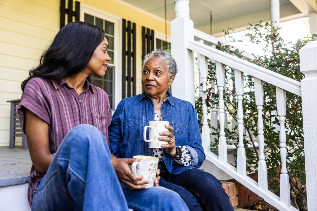 senior woman and adult daughter having coffee on front porch of rural farm home